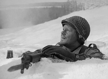 Movie still from “Battleground” (1949), directed by William A. Wellman – A soldier laying in the snow holding a rifle; Medium shot, Low angle