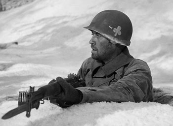 Movie still from “Battleground” (1949), directed by William A. Wellman – A man in a military uniform is holding a rifle; Medium shot, Low angle