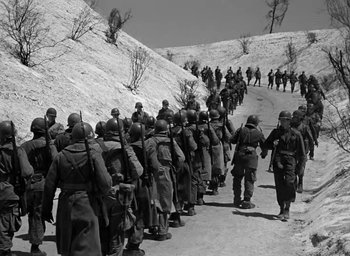 Movie still from “Battleground” (1949), directed by William A. Wellman – A black and white photo of a group of soldiers marching down a hill; Wide shot, High angle