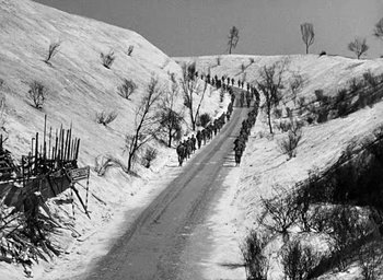 Movie still from “Battleground” (1949), directed by William A. Wellman – A black and white photo of a group of people walking down a snowy road; Extreme Wide shot, High angle