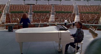 Movie still from “Beaches” (1988), directed by Garry Marshall – A man sitting at a piano in an empty stadium; Extreme Wide shot, High angle