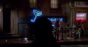 Movie still from “Beaches” (1988), directed by Garry Marshall – A person standing in front of a building with a neon cocktail sign; Wide shot, Over the shoulder angle