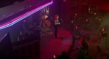 Movie still from “Beaches” (1988), directed by Garry Marshall – A woman standing on a stage singing into a microphone; Wide shot, High angle