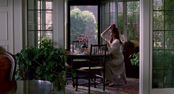Movie still from “Beaches” (1988), directed by Garry Marshall – A woman sitting at a dining room table; Wide shot, High angle