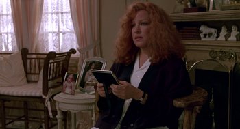Movie still from “Beaches” (1988), directed by Garry Marshall – A woman sitting in front of a table holding a book; Medium shot, Over the shoulder angle