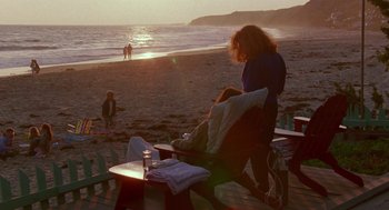 Movie still from “Beaches” (1988), directed by Garry Marshall – A woman sitting on a chair on the beach at sunset; Wide shot, High angle
