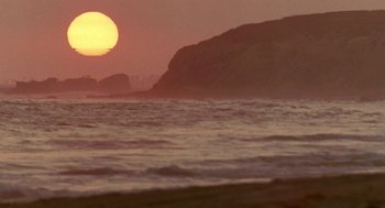 Movie still from “Beaches” (1988), directed by Garry Marshall – The sun is setting over the ocean with a mountain in the background; Extreme Wide shot, Low angle
