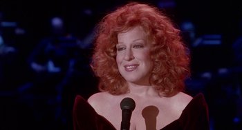 Movie still from “Beaches” (1988), directed by Garry Marshall – Bette midler in a red dress with a microphone in front; Close Up shot, Over the shoulder angle