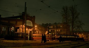 Two people walking down a street at night near a train station