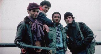 Movie still from “Beat Street” (1984), directed by Stan Lathan – A group of men standing next to each other holding skateboards; Medium shot, Low angle