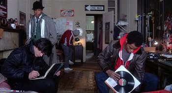 Movie still from “Beat Street” (1984), directed by Stan Lathan – A group of people sitting in a room; Medium shot, High angle