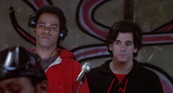 Movie still from “Beat Street” (1984), directed by Stan Lathan – Two young men are listening to music in front of a microphone in front of a mural; Close Up shot, Low angle