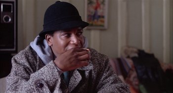 Movie still from “Beat Street” (1984), directed by Stan Lathan – A man wearing a hat and a jacket eating a sandwich; Close Up shot, Over the shoulder angle