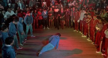 Movie still from “Beat Street” (1984), directed by Stan Lathan – A crowd of people watching a man do a break dance move; Wide shot, High angle