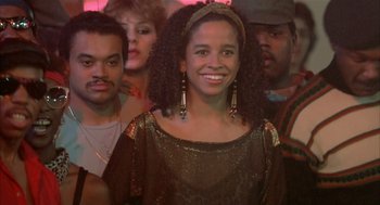 Movie still from “Beat Street” (1984), directed by Stan Lathan – A group of people standing in a room with a woman smiling; Close Up shot, Low angle