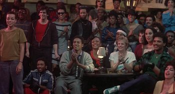 Movie still from “Beat Street” (1984), directed by Stan Lathan – A group of people sitting and standing in front of a microphone; Wide shot, High angle