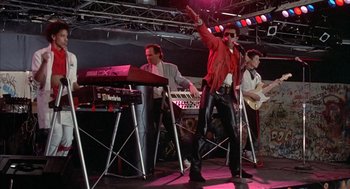 Movie still from “Beat Street” (1984), directed by Stan Lathan – A group of men standing on a stage with microphones; Wide shot, Low angle