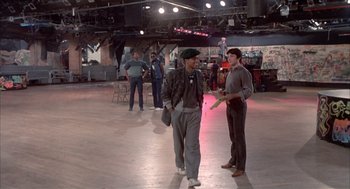 Movie still from “Beat Street” (1984), directed by Stan Lathan – A group of people standing around in a room; Wide shot, High angle