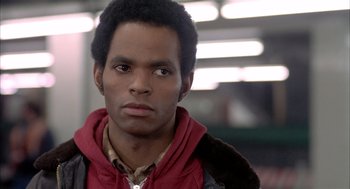 Movie still from “Beat Street” (1984), directed by Stan Lathan – A young man with a black coat is looking at the camera; Close Up shot, Over the shoulder angle