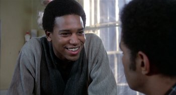 Movie still from “Beat Street” (1984), directed by Stan Lathan – A young man smiling while sitting next to another young man; Close Up shot, Over the shoulder angle