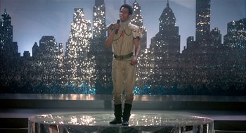 Movie still from “Beat Street” (1984), directed by Stan Lathan – A man standing on a stage holding a microphone; Wide shot, Low angle