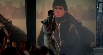 Movie still from “Beat Street” (1984), directed by Stan Lathan – A man standing in front of a large picture of a man; Medium shot, Low angle