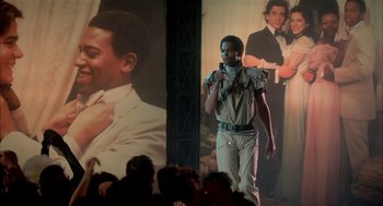 Movie still from “Beat Street” (1984), directed by Stan Lathan – A man standing in front of a large picture of a man; Medium shot, Low angle
