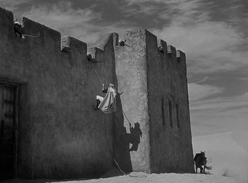 Movie still from “Beau Geste” (1939), directed by William A. Wellman – A man climbing up the side of a castle wall; Extreme Wide shot, Low angle