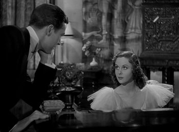 Movie still from “Beau Geste” (1939), directed by William A. Wellman – A man and a woman sitting at a table in front of a lamp; Medium shot, High angle