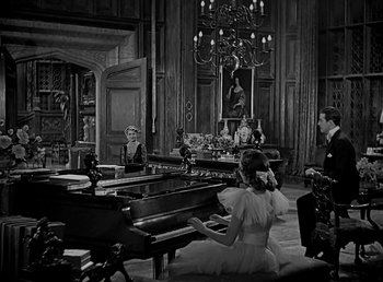 Movie still from “Beau Geste” (1939), directed by William A. Wellman – A black and white photo of a woman sitting at a piano in front of two men; Wide shot, High angle