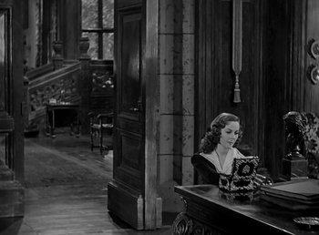 Movie still from “Beau Geste” (1939), directed by William A. Wellman – A black and white photo of a woman sitting at a table; Wide shot, High angle