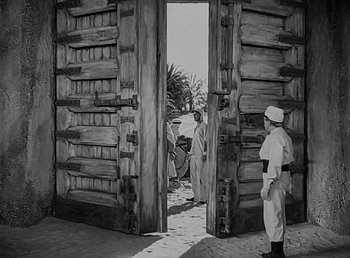 Movie still from “Beau Geste” (1939), directed by William A. Wellman – A black - and - white photo of two men standing in front of an open door; Wide shot, Low angle
