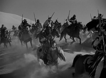 Movie still from “Beau Geste” (1939), directed by William A. Wellman – A group of people riding horses through the desert; Wide shot, Low angle