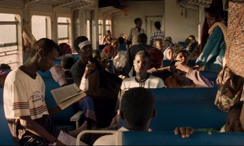 Movie still from “Beau Travail” (1999), directed by Claire Denis – A group of people sitting in a room; Wide shot, Over the shoulder angle