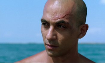 Movie still from “Beau Travail” (1999), directed by Claire Denis – A man with a shaved head looking into the distance; Close Up shot, Low angle