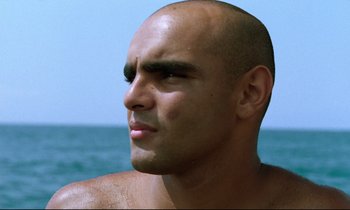 Movie still from “Beau Travail” (1999), directed by Claire Denis – A man with a shaved head looks into the distance; Close Up shot, Low angle