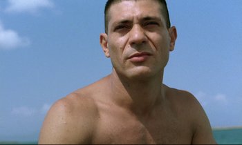 Movie still from “Beau Travail” (1999), directed by Claire Denis – A shirtless man with no shirt is posing for a picture; Close Up shot, Low angle