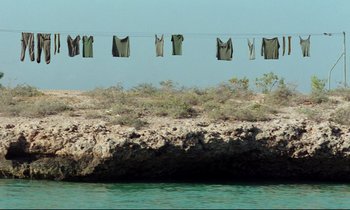 Movie still from “Beau Travail” (1999), directed by Claire Denis – Clothes are hanging on a clothes line over the water; Extreme Wide shot, Low angle