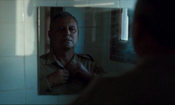 Movie still from “Beau Travail” (1999), directed by Claire Denis – An older man looking in the mirror in front of a window; Close Up shot, Over the shoulder angle