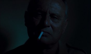 Movie still from “Beau Travail” (1999), directed by Claire Denis – An older man is smoking a cigarette in the dark; Close Up shot, Low angle