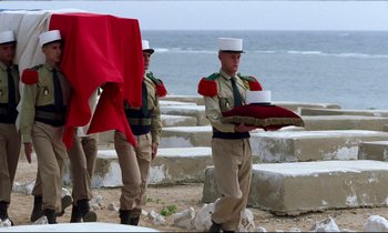 Movie still from “Beau Travail” (1999), directed by Claire Denis – A group of men standing next to each other near the ocean; Wide shot, High angle