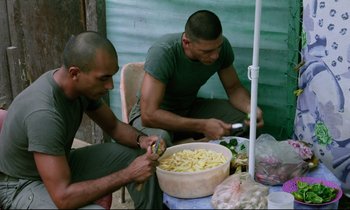 Movie still from “Beau Travail” (1999), directed by Claire Denis – A couple of men sitting next to a bowl of food; Medium shot, High angle