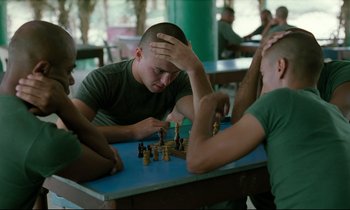 Movie still from “Beau Travail” (1999), directed by Claire Denis – A group of men sitting at a table playing chess; Close Up shot, High angle