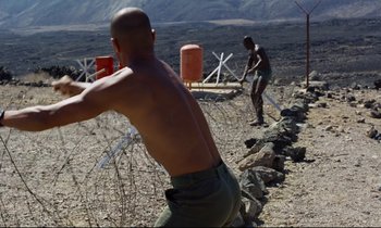 Movie still from “Beau Travail” (1999), directed by Claire Denis – Two men are playing frisbee on the beach; Wide shot, Over the shoulder angle
