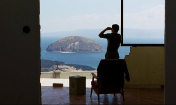 Movie still from “Beau Travail” (1999), directed by Claire Denis – A person sitting on a chair looking out a window at the ocean; Extreme Wide shot, Over the shoulder angle