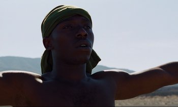 Movie still from “Beau Travail” (1999), directed by Claire Denis – A man with a bandage on his head is standing in the desert; Close Up shot, Low angle