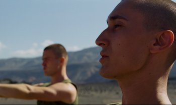 Movie still from “Beau Travail” (1999), directed by Claire Denis – Two young men are standing in the desert; Close Up shot, Low angle