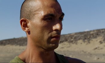 Movie still from “Beau Travail” (1999), directed by Claire Denis – A man's face in the desert; Close Up shot, Low angle