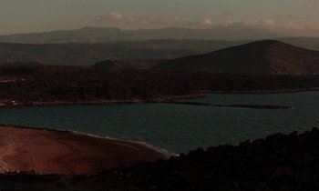 Movie still from “Beau Travail” (1999), directed by Claire Denis – A body of water surrounded by mountains at night; Extreme Wide shot, High angle