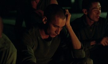 Movie still from “Beau Travail” (1999), directed by Claire Denis – A man sitting in the dark with his head resting on his hand; Close Up shot, Over the shoulder angle